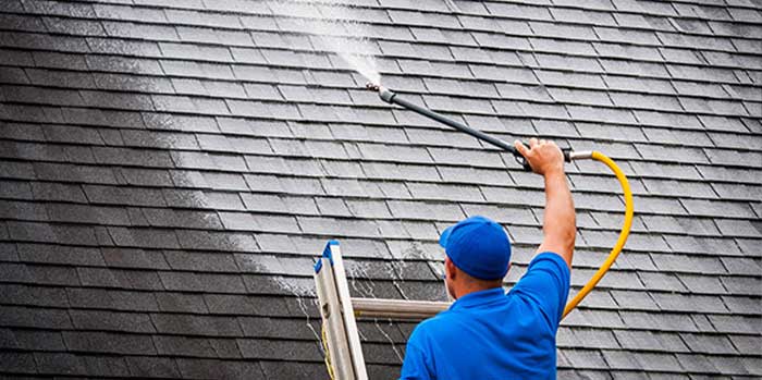 Roofer cleaning an asphalt roof with a pressure washer. 
